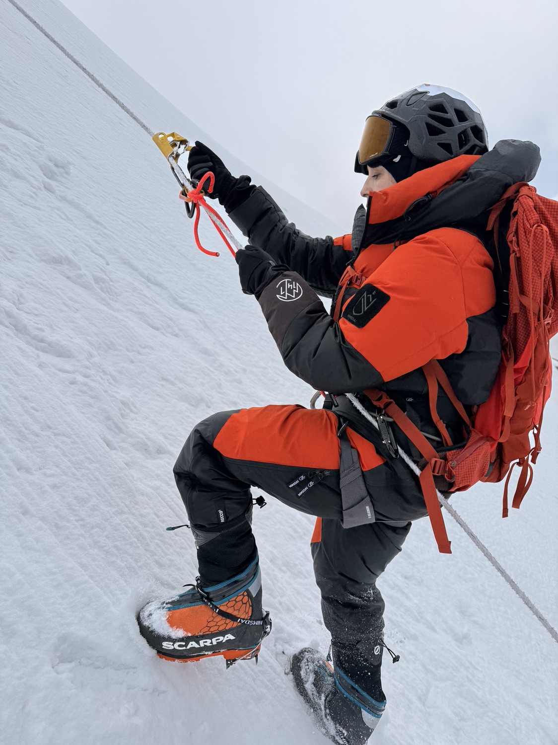 Adriana Aristizábal asciende por una cuerda fija en las laderas nevadas del Lobuche Peak, con casco, gafas y traje naranja de expedición